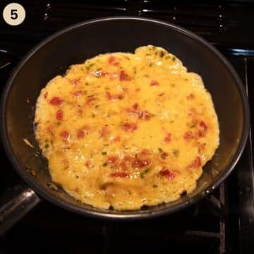 cooking chili omelet with tomatoes in a small frying pan.