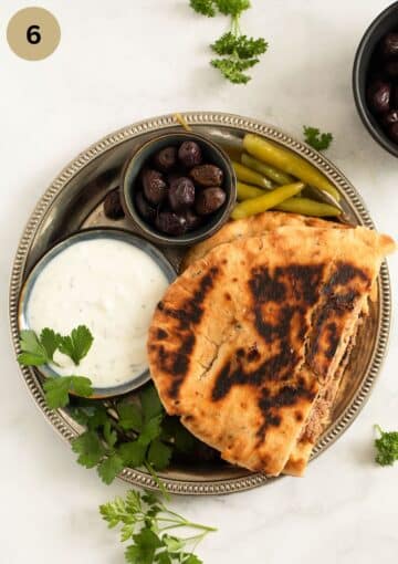 a plate with lamb arayes, yogurt dip, olives, and pickled hot peppers.