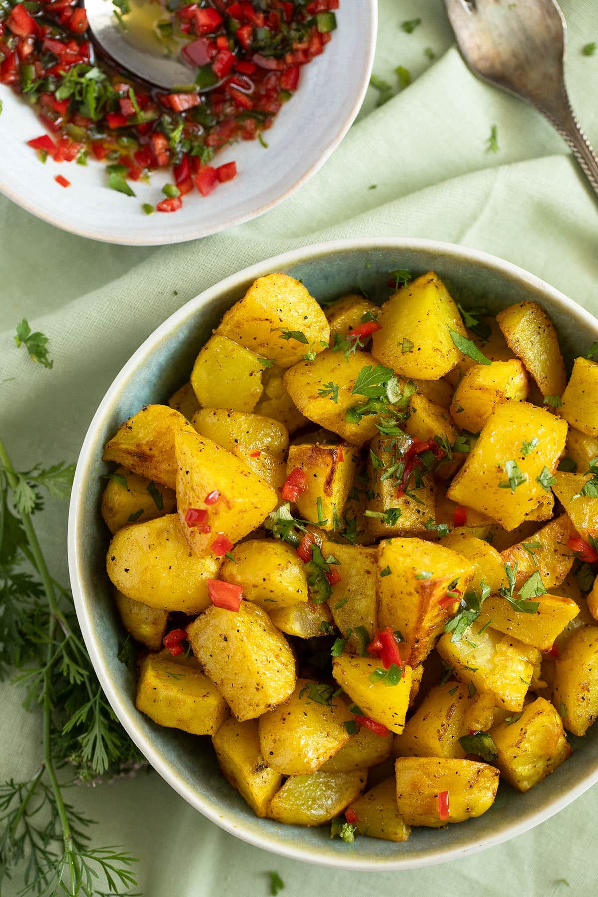 lebanese style potatoes drizzled with chili sauce in a bowl, another bowl with more sauce beside it.