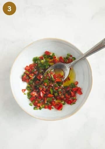 red and green fresh chili sauce with oil and cilantro in a small bowl with a spoon.