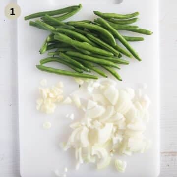 trimmed fresh green beans and sliced onions on a cutting board.