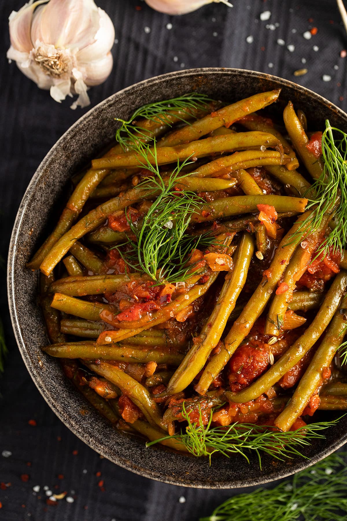 stewed green beans topped with fresh dill on a plate, a bulb of garlic on the side.