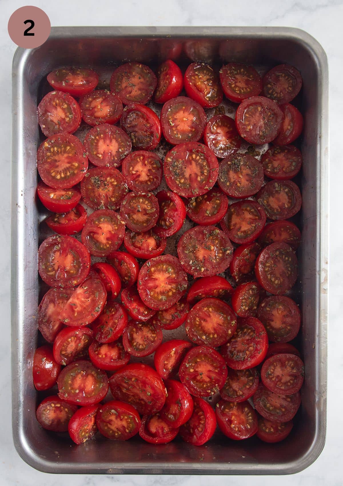 halved and seasoned tomatoes in a baking pan before roasting.
