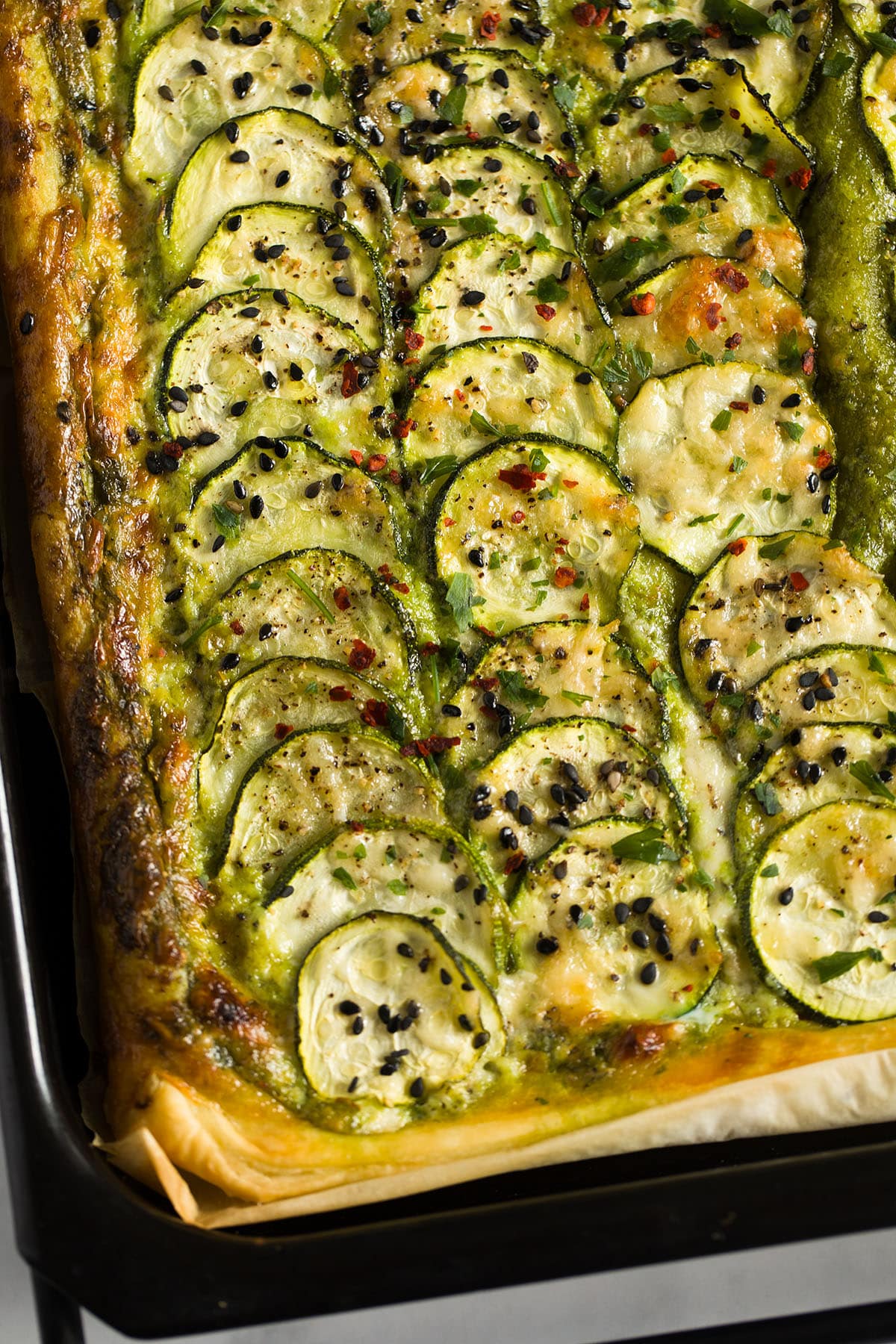 zucchini tart with puff pastry, mascarpone filling and parmesan on a baking tray.