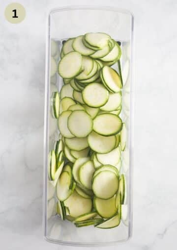 thin zucchini slices in the rectangular container of a mandoline.