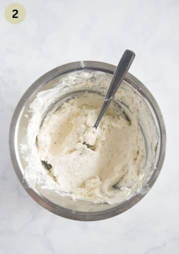 stirring mascarpone with sour cream, garlic and seasoning with a spoon in a bowl.