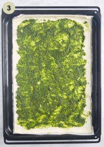 puff pastry on a baking sheet with a layer of green pesto spread evenly over it.