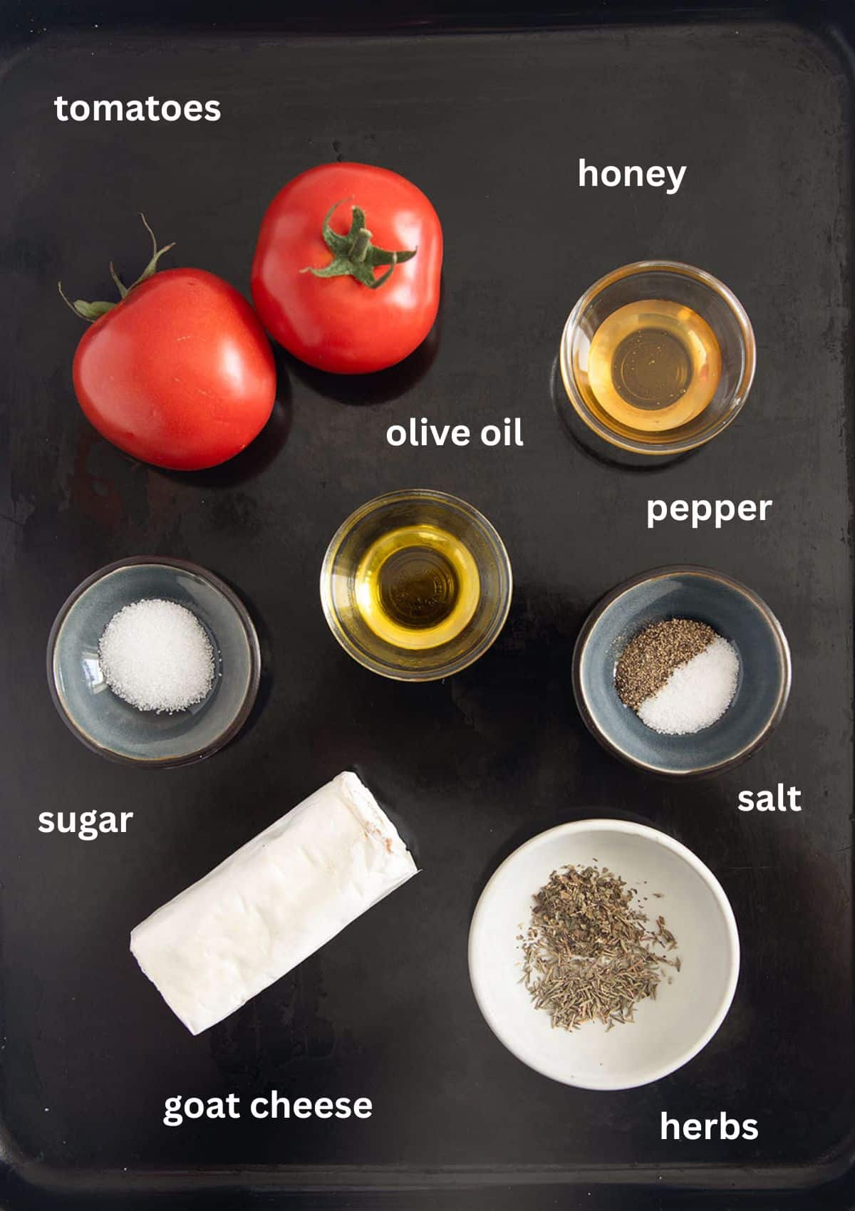 labeled ingredients for baking goat cheese on tomatoes with oil, honey, sugar, and herbs.
