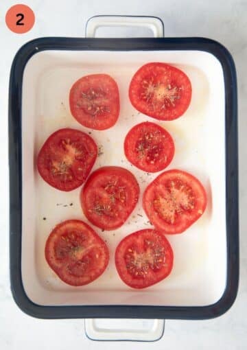 large tomato slices drizzled with seasoning in a roasting tin.