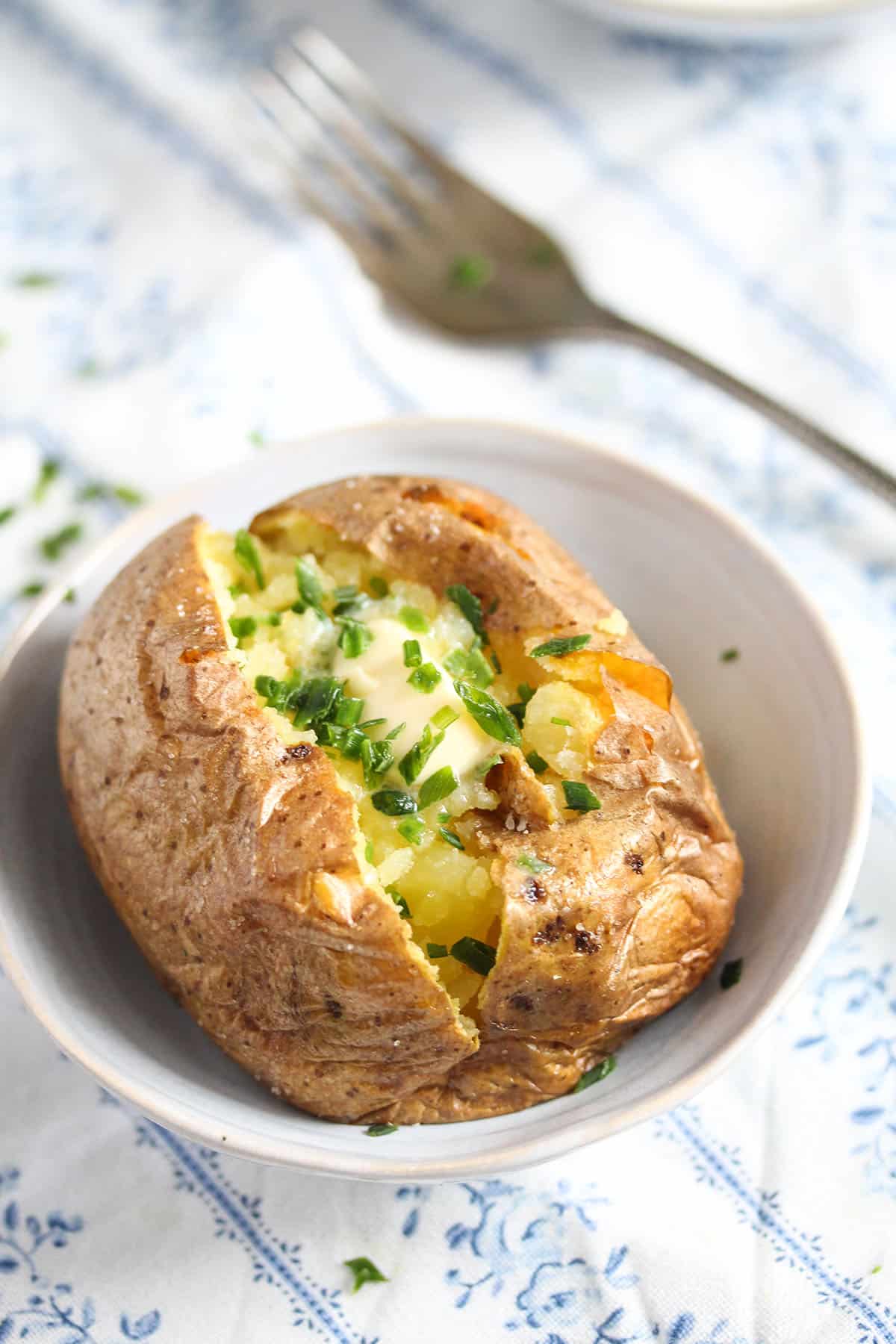 one baked potato in a bowl served with melted butter and fresh chives.