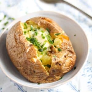 baked potato with butter and chives in a small serving bowl.