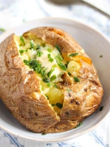 baked potato with butter and chives in a small serving bowl.