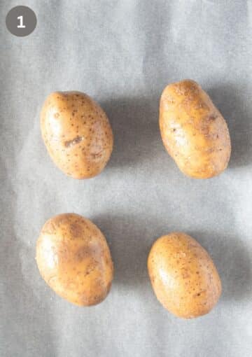four large and seasoned potatoes on a baking sheet before baking.