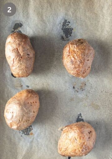 four large baked potatoes on a baking sheet.