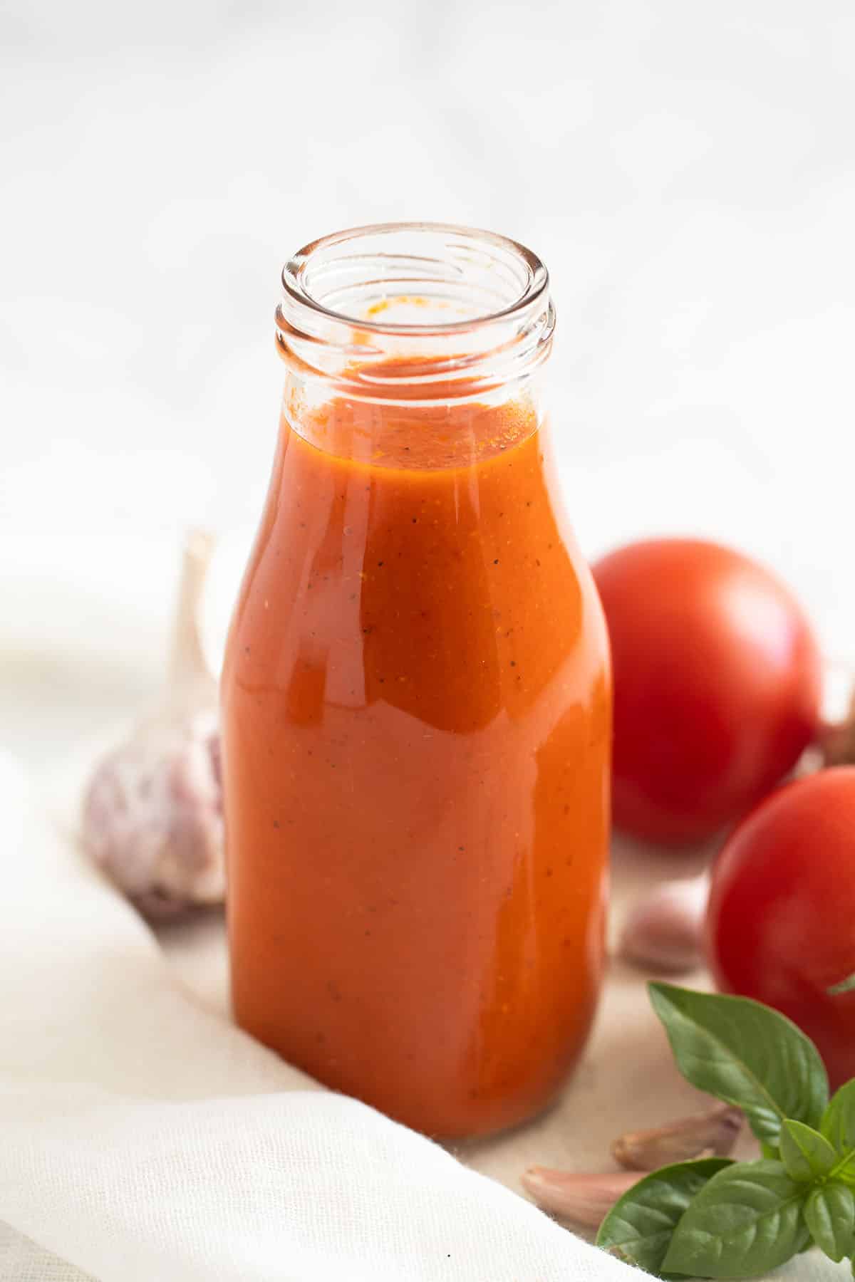 a bottle of homemade ketchup, two fresh tomatoes, and basil leaves .
