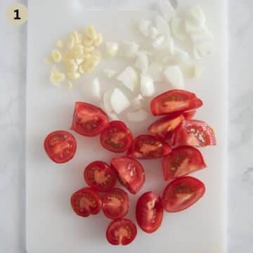 quartered tomatoes and sliced onions and garlic on a cutting board.