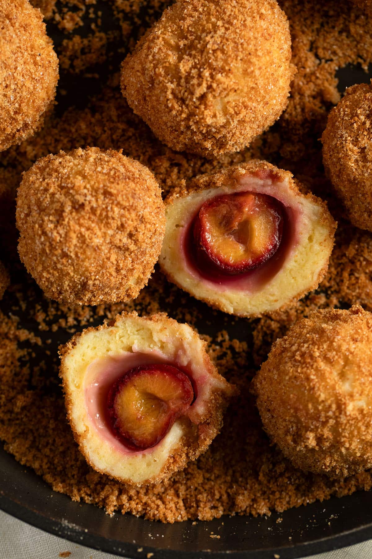 eastern european plum dumplings coated with breadcrumbs, one cut in the middle to show the plum inside.
