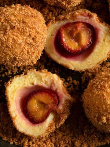 plum dumplings with breadcrumb coating, one cut in the middle to show the plum.