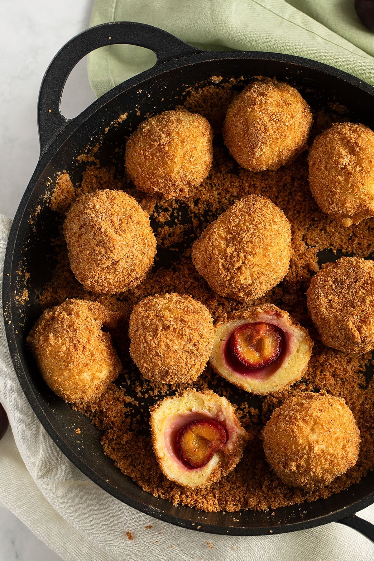 many small plum dumplings coated in breadcrumbs in a cast iron skillet, one cut in the middle. 