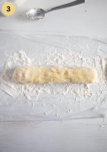 a log of dough for dumplings on a floured pieces of plastic wrap and a teaspoon beside it.