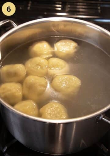 plum dumplings simmering in a large pot full of hot water.
