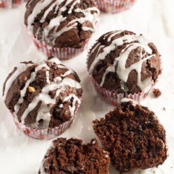 three cocoa pumpkin muffins drizzled with glaze and one halved to show the moist crumb.