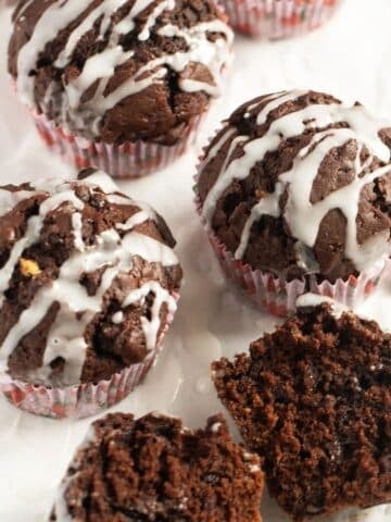 three cocoa pumpkin muffins drizzled with glaze and one halved to show the moist crumb.