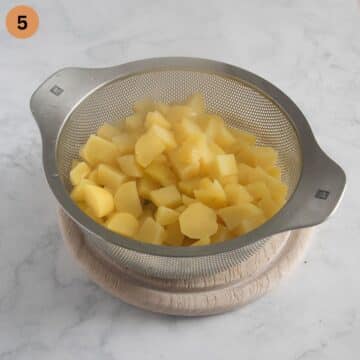 cooked chopped potatoes for making mash in a sieve.