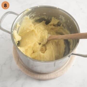 stirring mashed potatoes in a large pot with a wooden spoon.