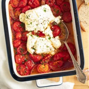 roasted tomatoes and feta in a small baking dish with a spoon in it.