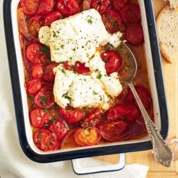 roasted tomatoes and feta in a small baking dish with a spoon in it.