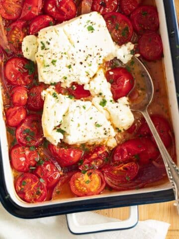 roasted tomatoes and feta in a small baking dish with a spoon in it.