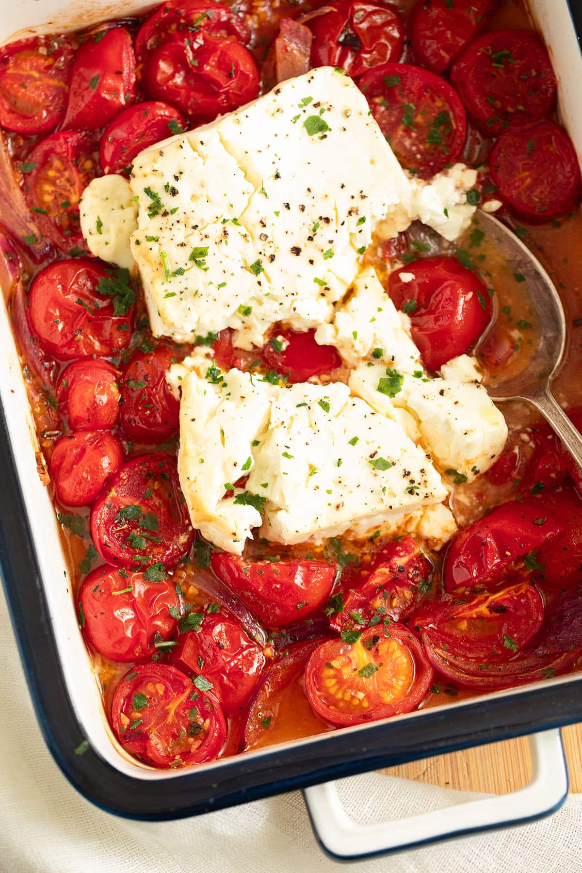 one large piece of baked feta broken in the middle on a bed of roasted tomatoes.