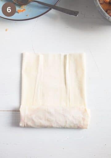rolling a filo parcel stuffed with chicken and veggies on the table.