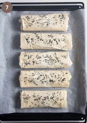 five unbaked filo chicken parcels on a baking sheet lined with parchment paper.