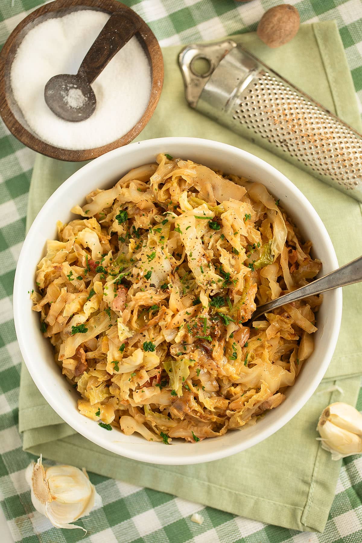 a bowl of german savoy cabbage, one with salt, garlic cloves and a nutmeg grater on the table.