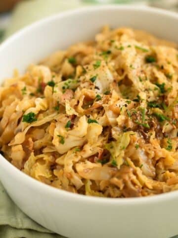 creamy savoy cabbage with bacon and parsley piled in a white bowl.
