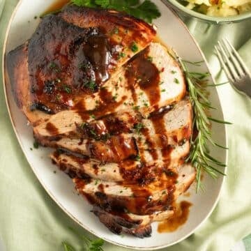 honey baked turkey breast sliced on a platter and drizzled with sauce.
