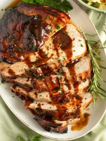 honey baked turkey breast sliced on a platter and drizzled with sauce.
