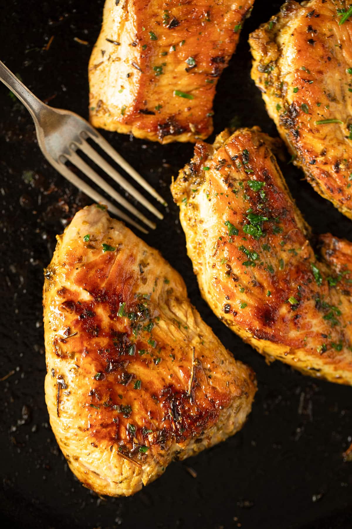 four golden and juicy turkey steak sprinkled with parsley and a fork.