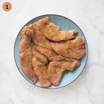 Raw turkey steaks on a cutting board, rubbed with oil and seasoned with poultry seasoning, salt and pepper.