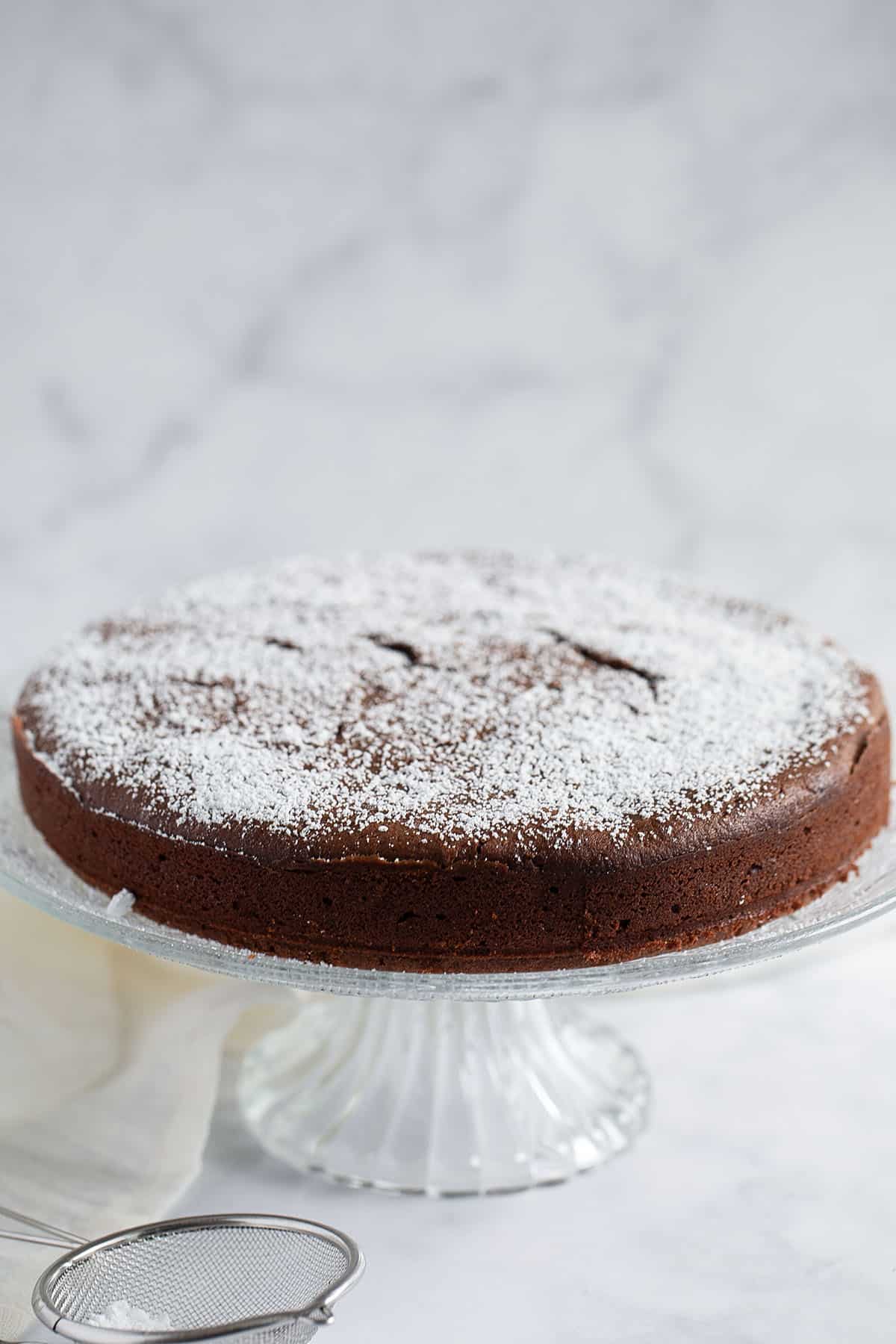 chocolate and ricotta cake dusted with confectioner's sugar on a tall cake platter.