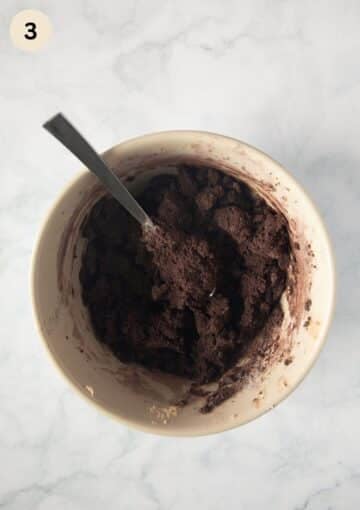 folding a cocoa and flour mixture into creamed butter and sugar in a bowl using a spoon.