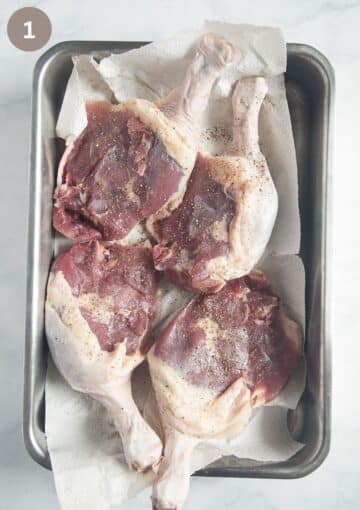 four raw and seasoned duck legs drying on paper towels.