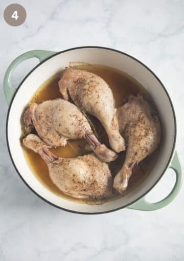 four half-cooked duck legs in cooking liquid in a dutch oven.