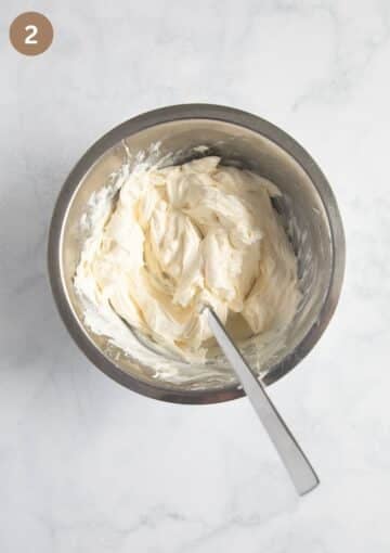 Cream cheese in a mixing bowl with sun-dried tomato oil being stirred until smooth and creamy.