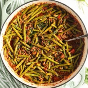 beef and green bean ragu in a dutch oven with a serving spoon in it.