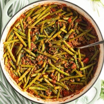 beef and green bean ragu in a dutch oven with a serving spoon in it.