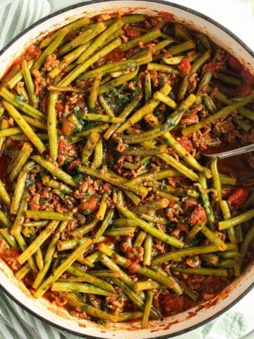 beef and green bean ragu in a dutch oven with a serving spoon in it.