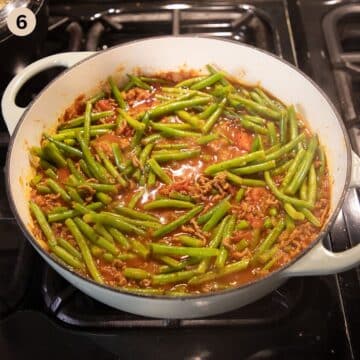simmering ragu with green beans, ground beef and tomatoes in a pot on the stove.